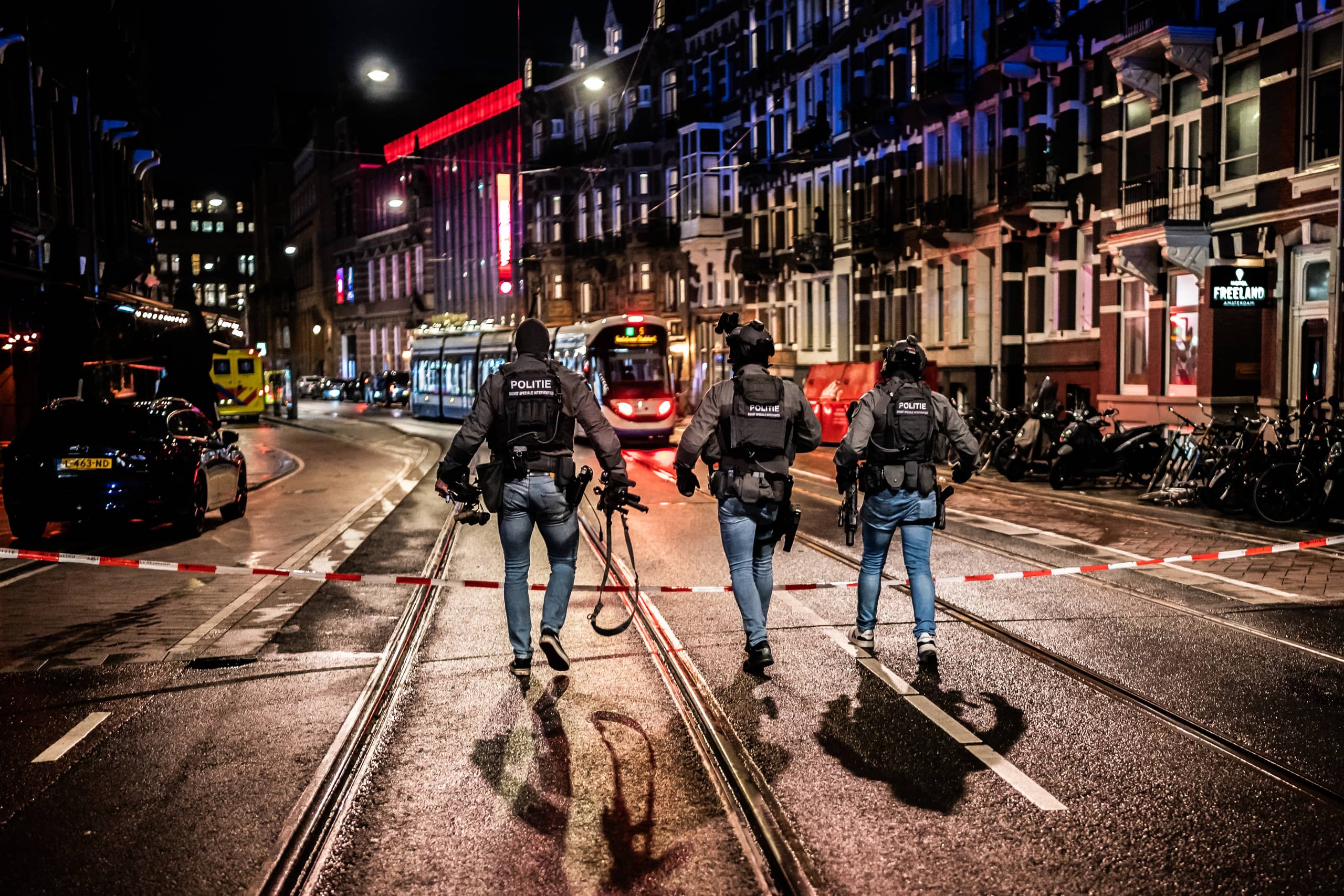 Straat in de avond in Amsterdam. Er lopen 3 mannen van de Dienst Speciale Interventies met volle wapenuitrusting, van achter gefotografeerd