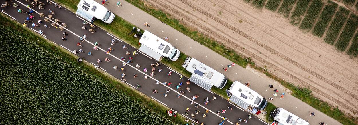 Een rij campers in de middenberm naast een wandelroute met diverse mensen van bovenaf gezien