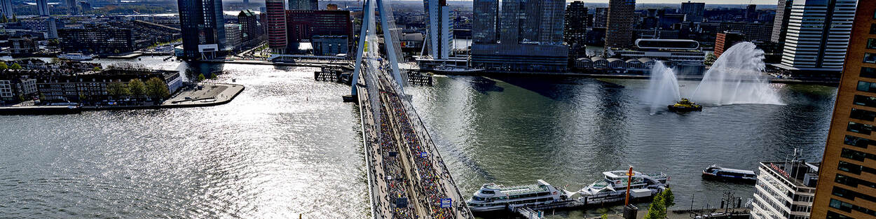 Erasmusbrug Rotterdam vanuit de lucht gezien tijdens de marathon met veel mensen op de burg en in het water boten die watershow geven