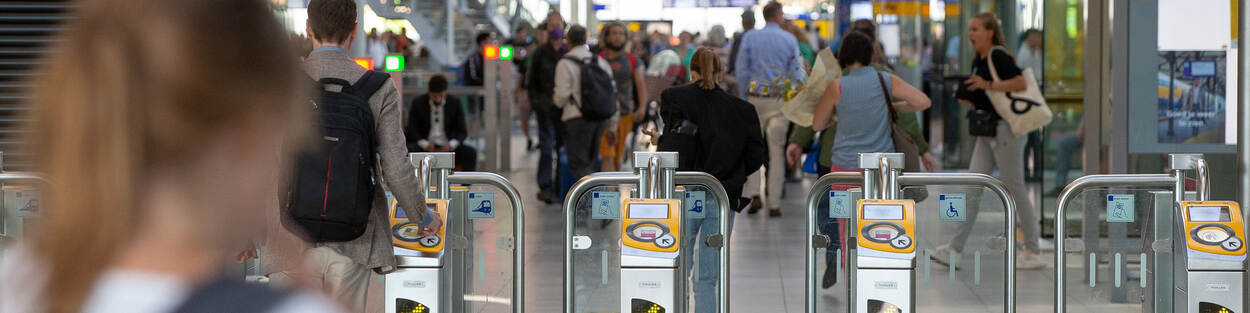 Diverse reizigers NS in een stationshal met in het midden een rij poortjes voor chipkaart controle