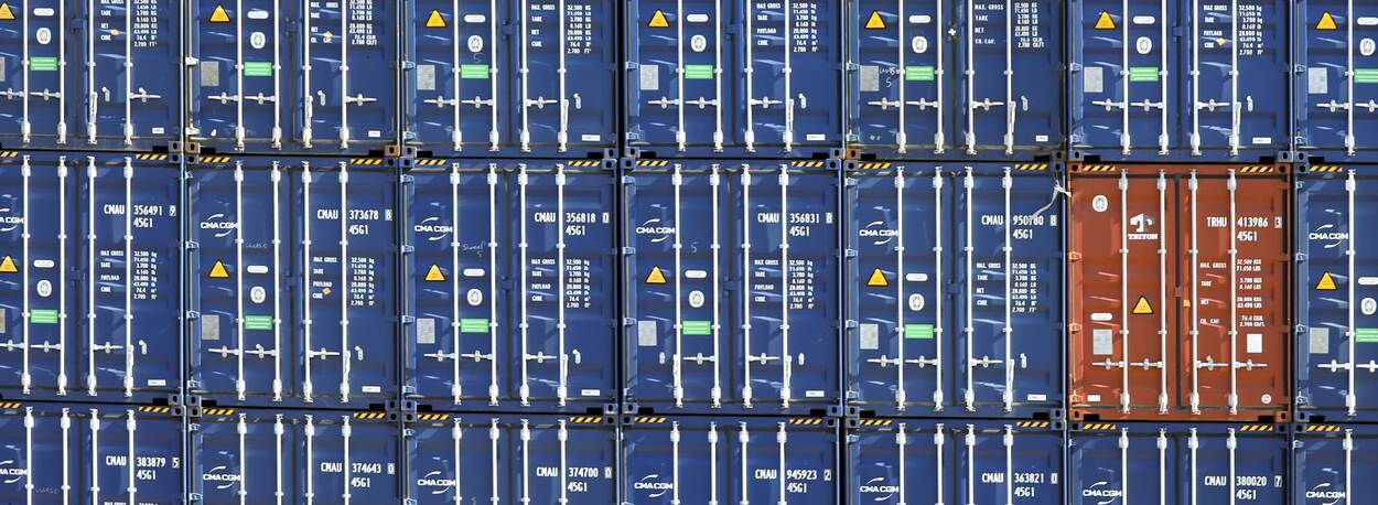 Diverse blauwe zeecontainers op elkaar gestapeld met een rode container ertussen
