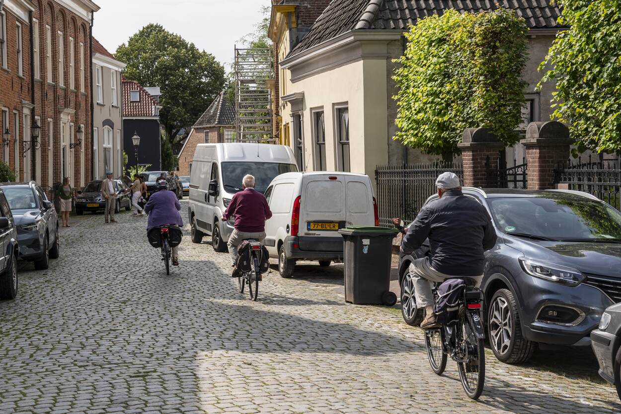 Mensen op de fiets in een straat in een wijkje met huizen en geparkeerde auto's