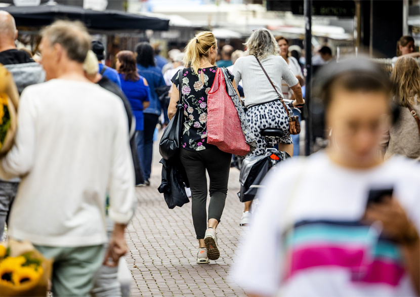 Mensen van achter gefotografeerd met boodschappentassen, op de fiets, kijkend op mobiel in een winkelstraat