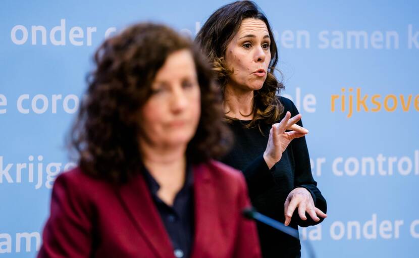 Gebarentolk Irma Sluijs is aan het gebarentolken tijdens persconferentie corona, zij staat op achtergrond en bewindspersoon schuin voor haar