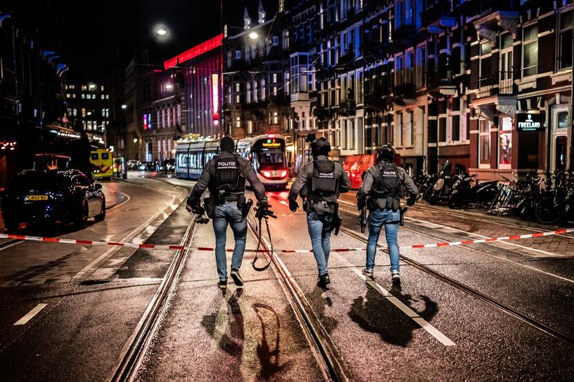 Straat in de avond in Amsterdam. Er lopen 3 mannen van de Dienst Speciale Interventies met volle wapenuitrusting, van achter gefotografeerd