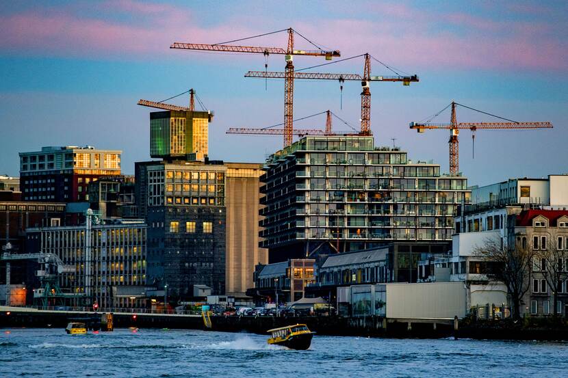 Een watertaxi op het water met op de achtergrond flatgebouwen en bouwkranen