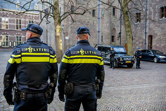 2 politieagenten op de rug gezien met verderop 2 KMar medewerkers met auto