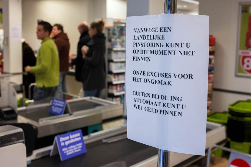 Mensen in de rij bij de kassa met daarbij opgehangen briefje over pinstoring