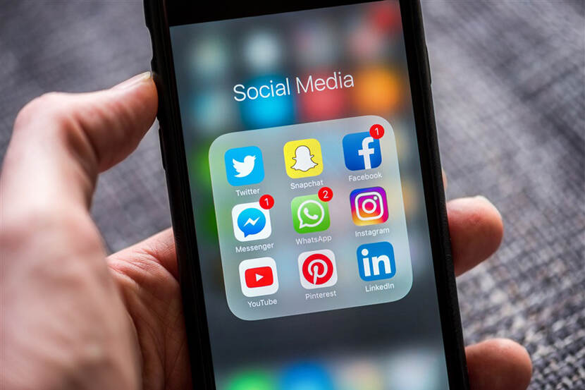 Iemand houdt een telefoon vast en daarop zijn social media apps te zien